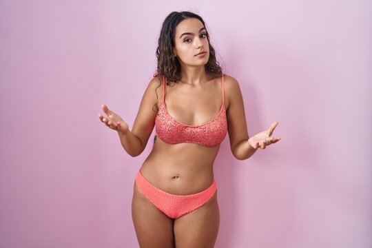 Young hispanic woman wearing lingerie over pink background clueless and confused with open arms, no idea concept.