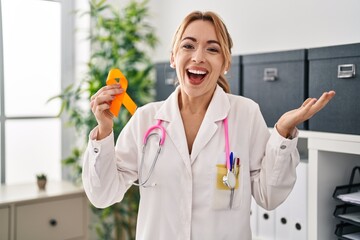 Hispanic doctor woman holding awareness orange ribbon celebrating victory with happy smile and...