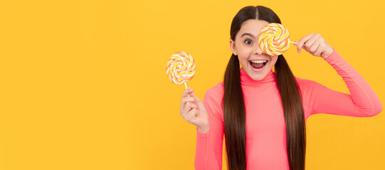 amazed teen girl with lollipop candy on stick on yellow background. Teenager child with sweets,...