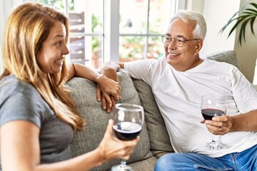 Middle age hispanic couple smiling happy drinking wine sitting on the sofa at home.