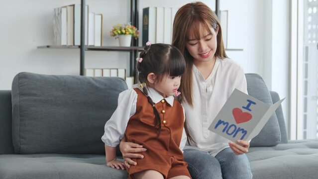 Young asia mother sitting on couch with child daughter reading fairy tales together. Child daughter reading book learning education fairy tale story bonding enjoying with mom in living room