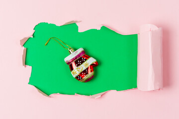 Red Christmas Decoration in Shape of Mitten Lying on Background with Hole Pink and Green Background