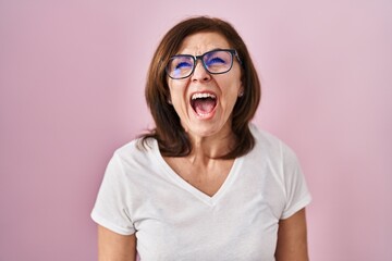 Middle age hispanic woman standing over pink background angry and mad screaming frustrated and furious, shouting with anger. rage and aggressive concept.