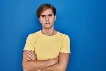 Young man standing over blue background skeptic and nervous, disapproving expression on face with crossed arms. negative person.