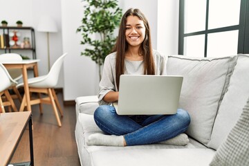 Young latin woman using laptop sitting on sofa at home