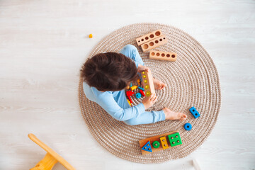 a kid in pajamas is sitting on the floor in his room and playing with a wooden construction kit. natural toys for children. the boy is playing in his bedroom.