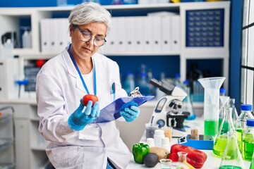 Middle age woman wearing scientist uniform holding tomatoe at laboratory