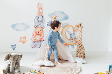 a little boy in a children's playroom with a wigwam and a giraffe playing with wooden toys with...