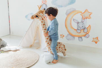 a little boy in a children's playroom with a wigwam and a giraffe playing with wooden toys with...