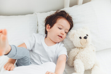 A little Asian boy in pajamas lying on the bed with a teddy bear, The child wakes up happy, The child wakes up early in the morning.natural bed linen for children
