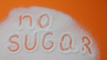 Word no sugar hand lettering on a placer of refined white sugar. Beet sugar crystals granules on a orange background