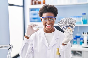 African american woman working at scientist laboratory holding dollars winking looking at the camera with sexy expression, cheerful and happy face.