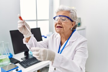 Senior grey-haired woman wearing scientist uniform using pipette and test tube at laboratory