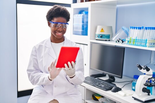 African american woman wearing scientist uniform using touchpad at laboratory