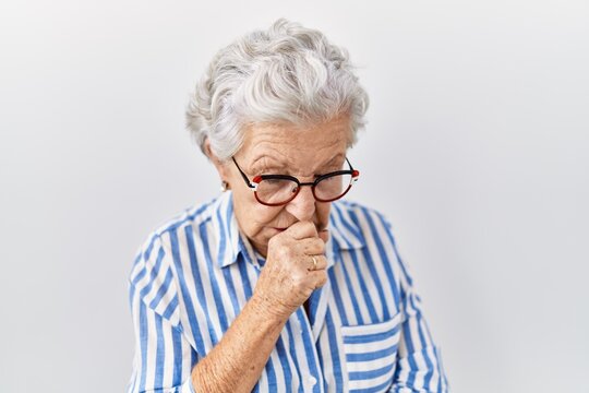 Senior woman with grey hair standing over white background feeling unwell and coughing as symptom for cold or bronchitis. health care concept.
