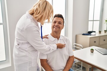 Fototapeta premium Middle age man and woman doctor and patient auscultating heart having medical consultation at clinic