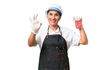 Butcher woman wearing an apron and serving fresh cut meat over isolated background showing ok sign with fingers