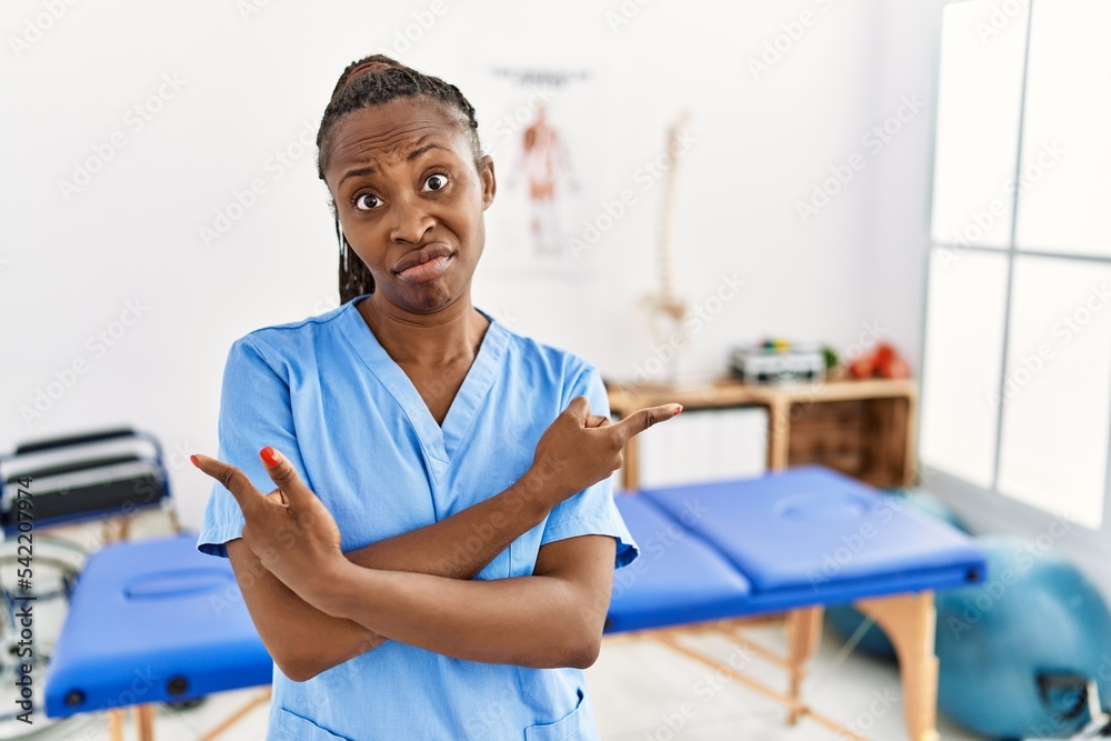 Canvas Prints Black woman with braids working at pain recovery clinic pointing to both sides with fingers, different direction disagree