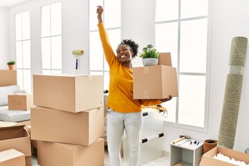 African american woman holding package standing with winner expression at new home