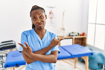 Black woman with braids working at pain recovery clinic pointing to both sides with fingers, different direction disagree