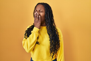 African woman standing over yellow background bored yawning tired covering mouth with hand. restless and sleepiness.