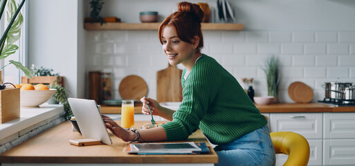 Beautiful young woman having lunch and using digital tablet while sitting at the kitchen counter