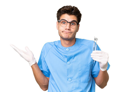 Young dentist man holding tools over isolated background having doubts while raising hands