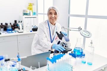 Fototapeta premium Middle age grey-haired woman wearing scientist uniform using microscope at laboratory