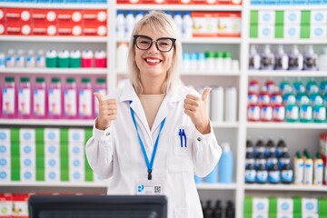 Young caucasian woman working at pharmacy drugstore success sign doing positive gesture with hand,...