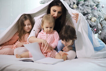 Fototapeta premium A family with children having fun on the bed under the covers during the Christmas holidays.