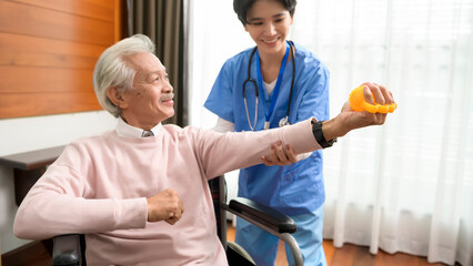 Asian nurse taking care of an elderly man sitting on wheelchair , doing hand exercises at  senior healthcare center.