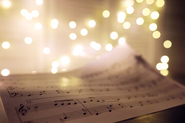 Old sheet with Christmas music notes as background against blurred lights. Christmas music concept