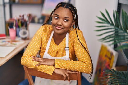 African american woman artist smiling confident sitting on chair at art studio