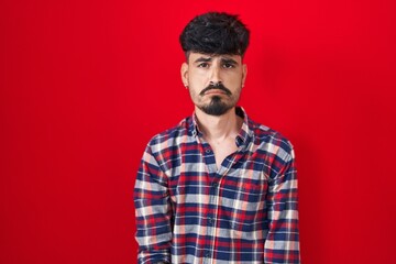 Young hispanic man with beard standing over red background depressed and worry for distress, crying angry and afraid. sad expression.