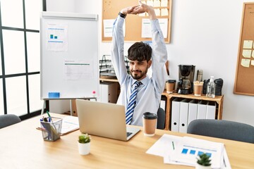 Young hispanic businessman tired stretching arms at the office.