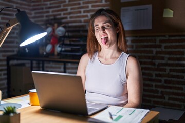 Brunette woman working at the office at night sticking tongue out happy with funny expression....