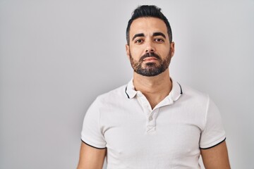 Young hispanic man with beard wearing casual clothes over white background relaxed with serious expression on face. simple and natural looking at the camera.
