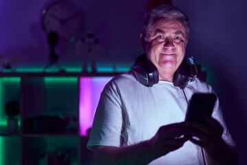 Middle age grey-haired man streamer using smartphone at gaming room