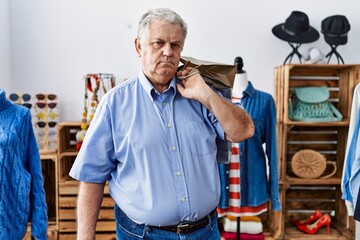 Senior man with grey hair holding shopping bags at retail shop thinking attitude and sober expression looking self confident