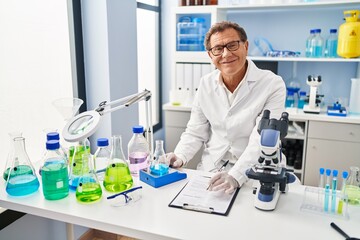 Middle age man wearing scientist uniform measuring test tube writing on clipboard at laboratory