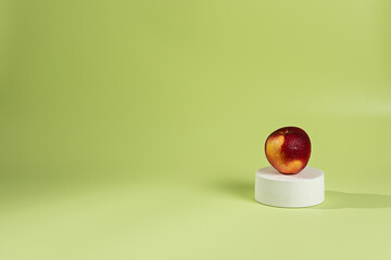 On one white podium top hat there is a red apple, a green background and a shadow from sunlight