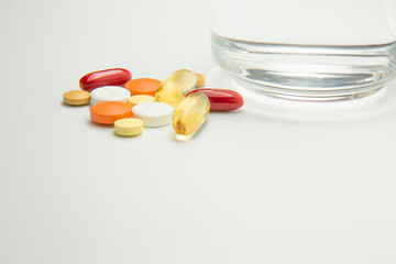 Colorful pills are lying near a glass of water. Medicines on a white background.