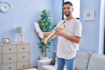 Young arab man musician holding trumpet and music sheet at home