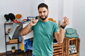 Young handsome man with beard holding shopping bags at retail shop doing italian gesture with hand and fingers confident expression