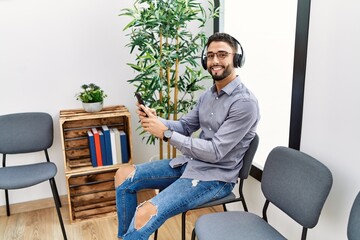 Fototapeta premium Young arab man listening to music sitting on chair at waiting room
