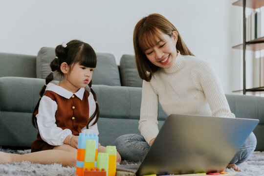 Mom and little 4 years old kid daughter with computer laptop playing education toy together at living room