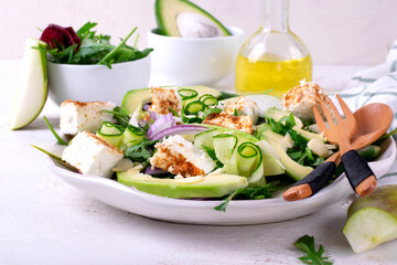 Salad with avocado, pear, cucumber, soft cheese and arugula served on the ceramic plate on white table
