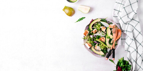 Web banner with salad with avocado, pear, cucumber, soft cheese and arugula served on the ceramic plate on white background. Top view. Mockup with copy space
