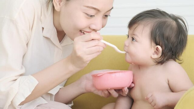 Young mother feeding her baby daughter eating with spoon.