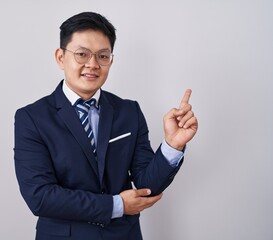 Young asian man wearing business suit and tie with a big smile on face, pointing with hand finger to the side looking at the camera.